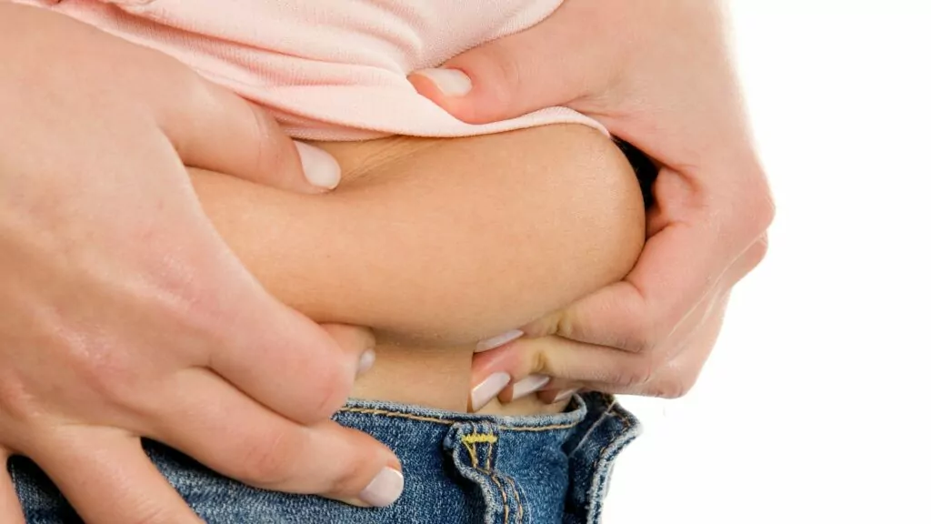 Femme touchant son ventre, symbolisant l'impact du stress sur le stockage de la graisse abdominale